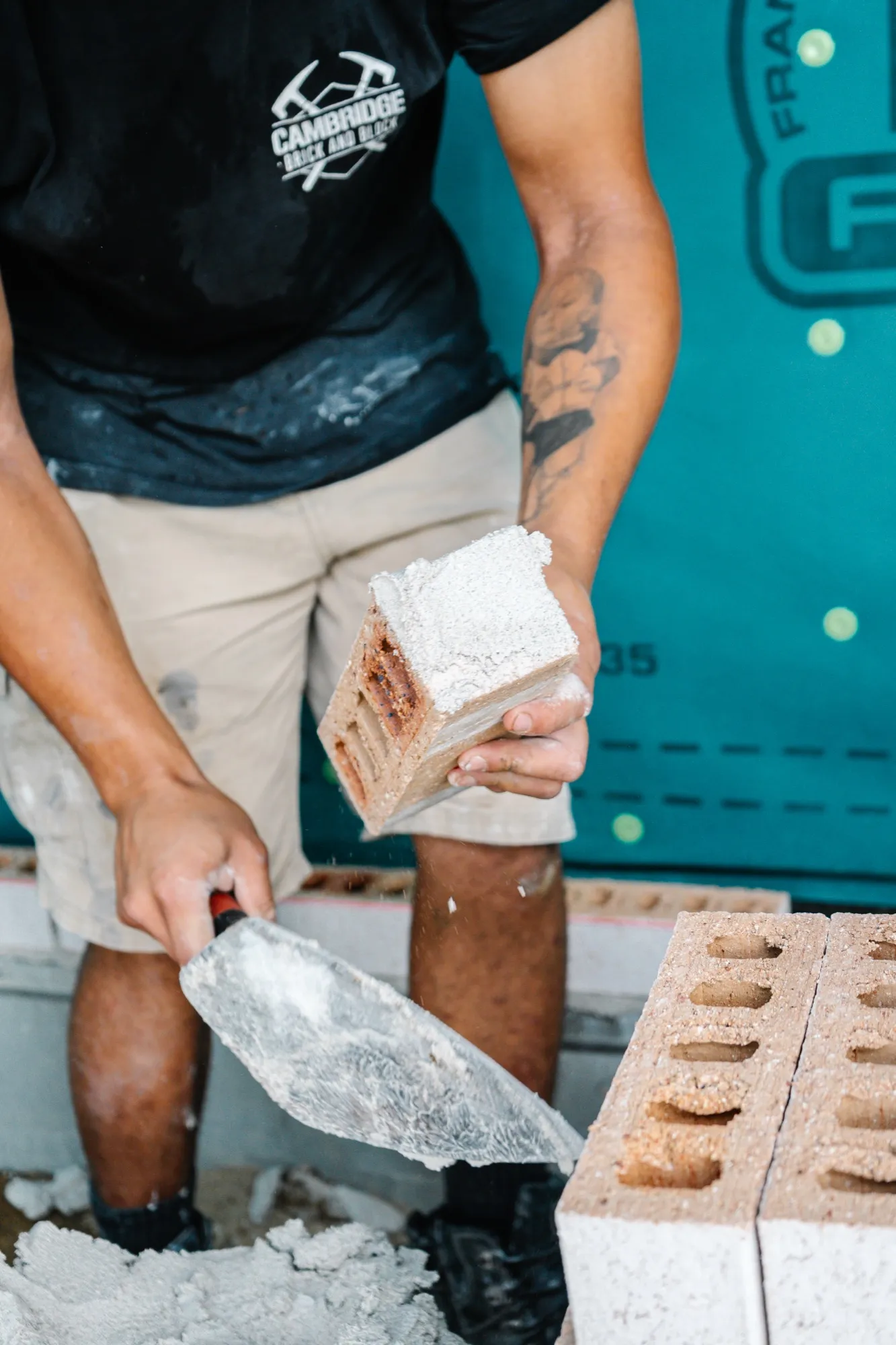 A bricklayer in a Cambridge Brick and Block shirt holding a brick and trowel