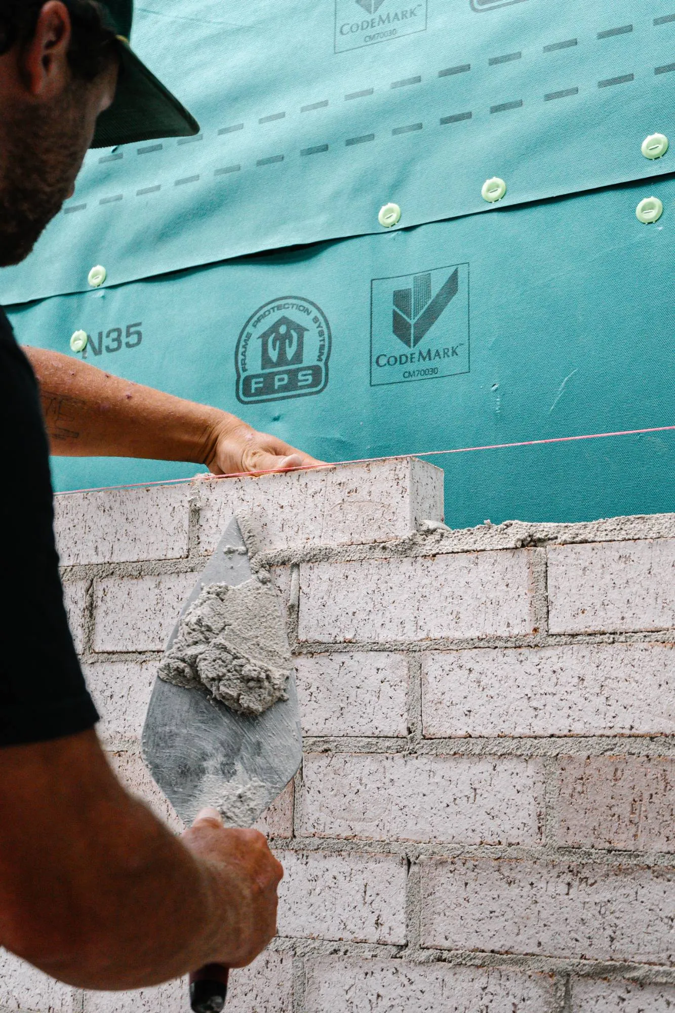 A Cambridge Brick and Block bricklayer setting a brick to the line, trowel loaded with mortar