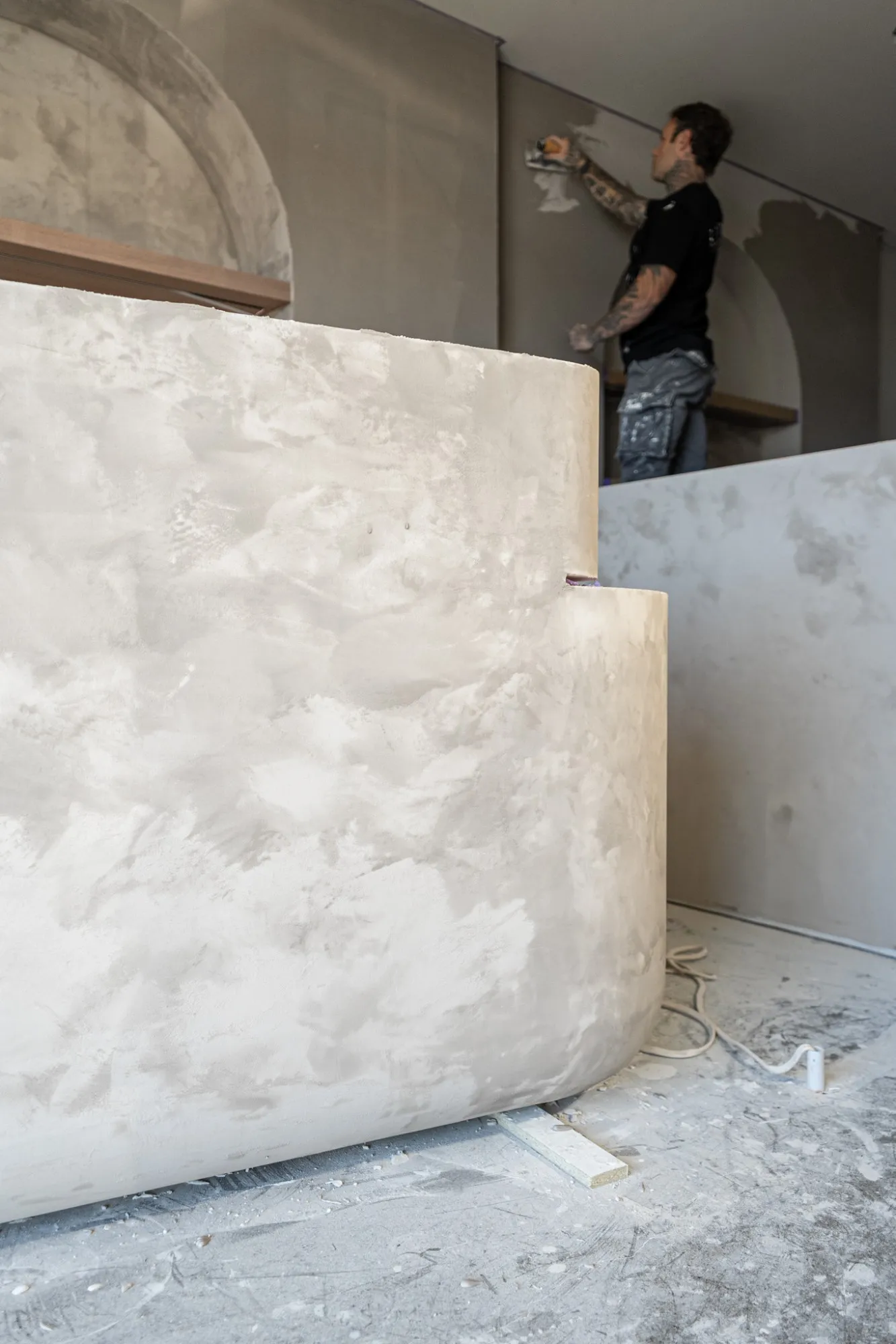 A finished curved plaster desk with the plasterer working on the wall behind